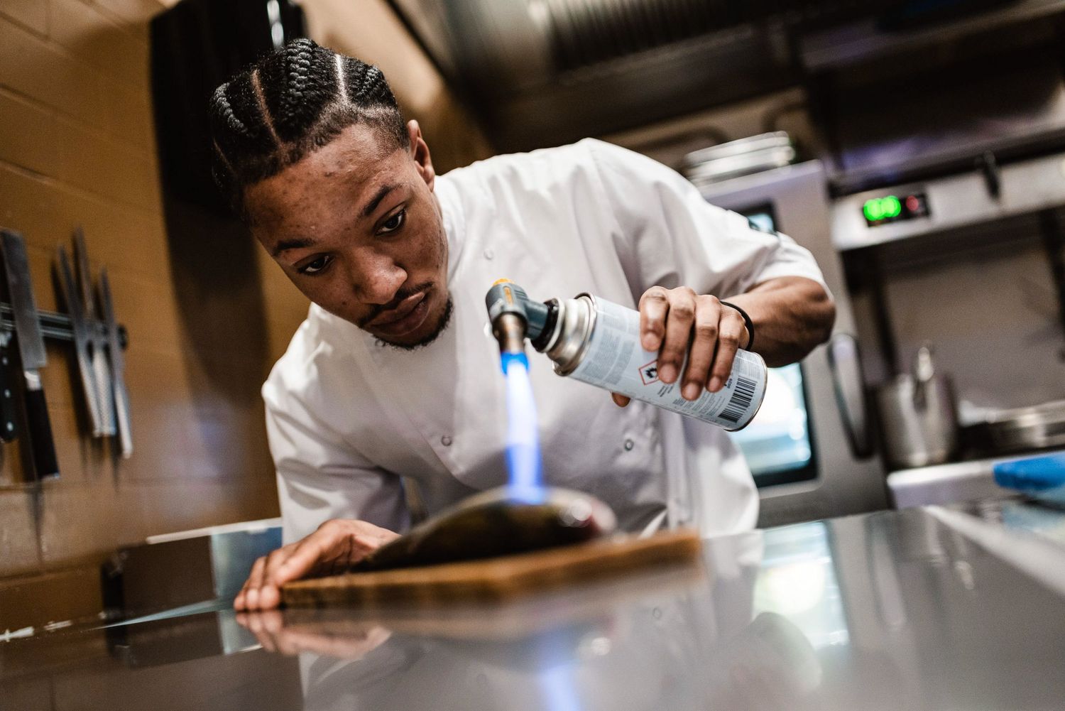 Chefs working in a professional kitchen lean over counters while preparing food with focused concentration.