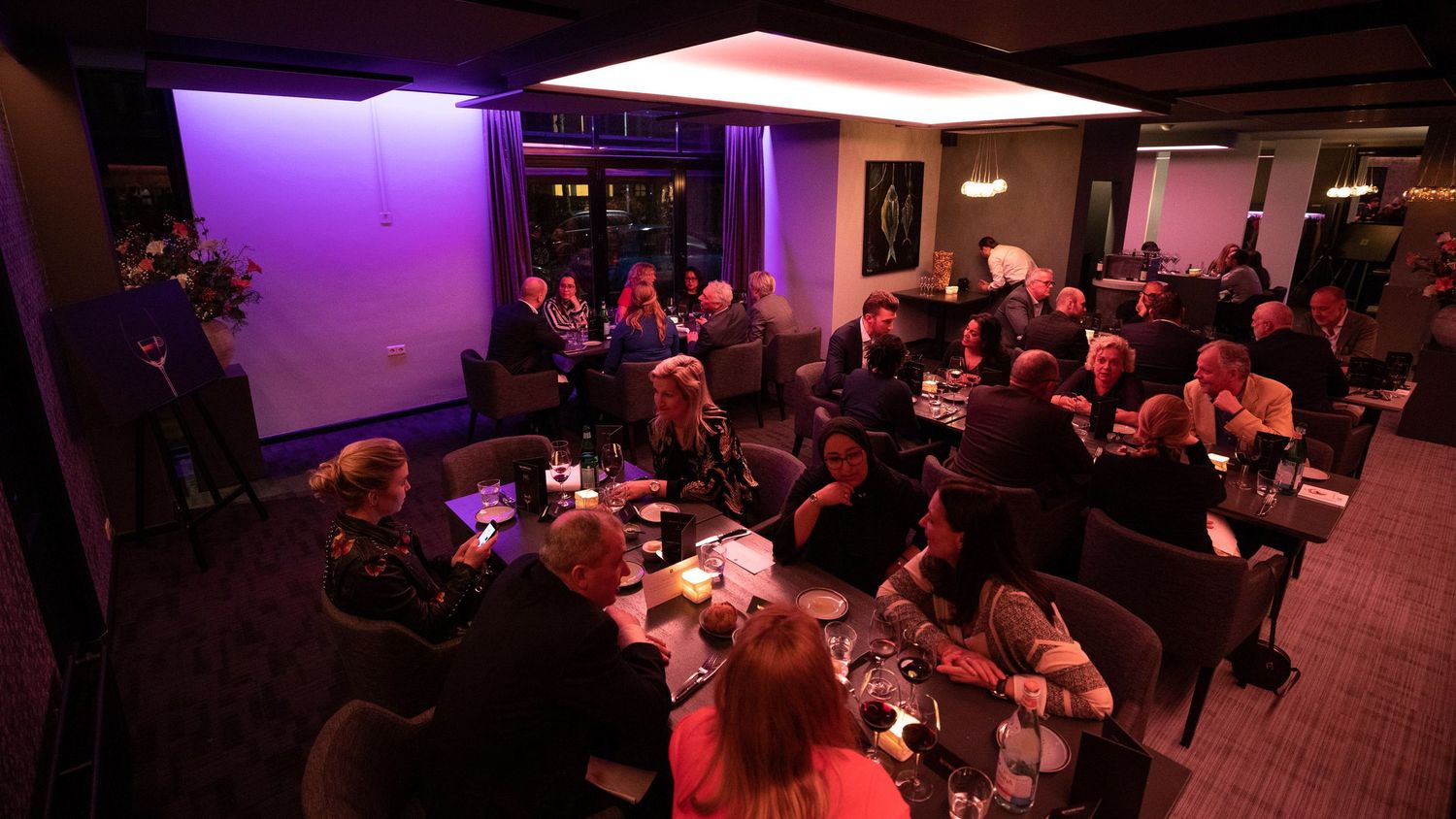Panoramic view of a crowded event space with purple and pink mood lighting.