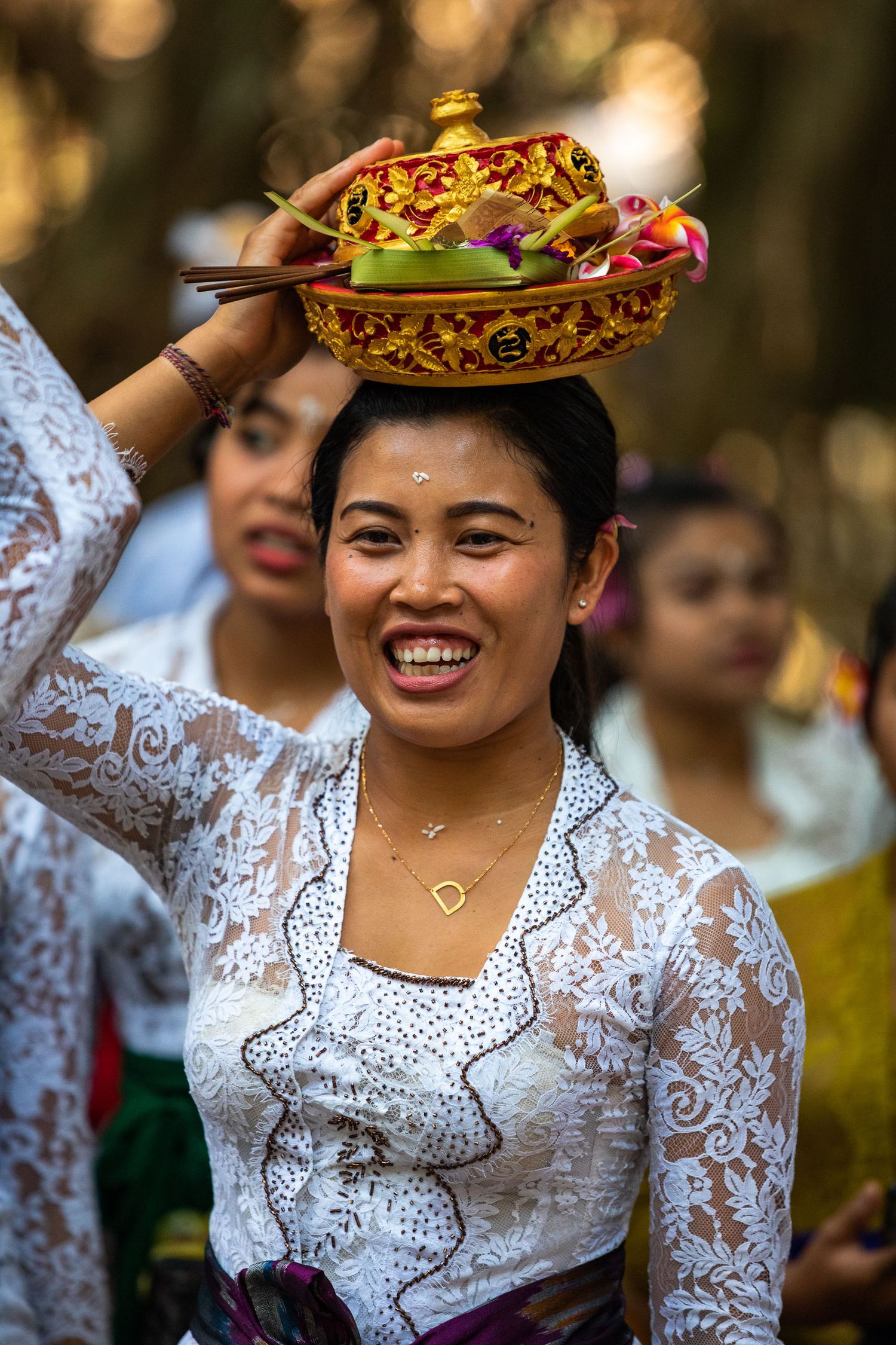 Woman in traditional white lace kebaya balancing decorative ceremonial offering during Balinese ritual.
