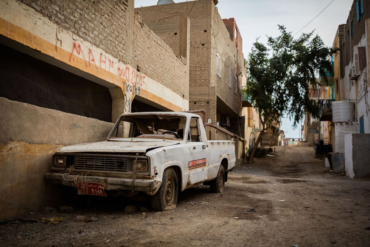 Vintage white pickup truck parked in a narrow alley between brick buildings.