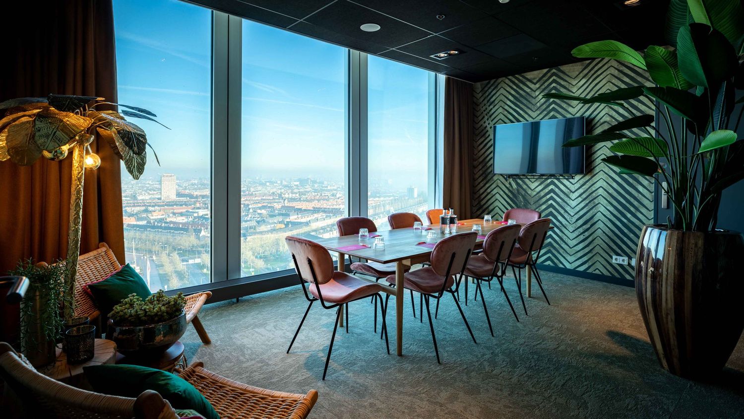 Modern office space with panoramic city views features sleek furniture, plants, and floor-to-ceiling windows.