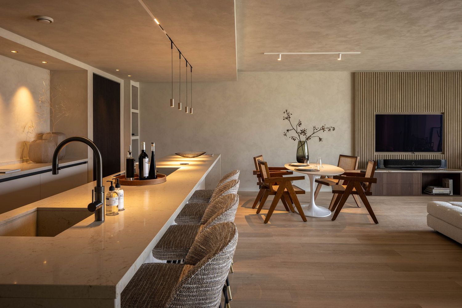 Modern open concept living room with concrete walls, track lighting, and contemporary furniture in warm neutral tones.