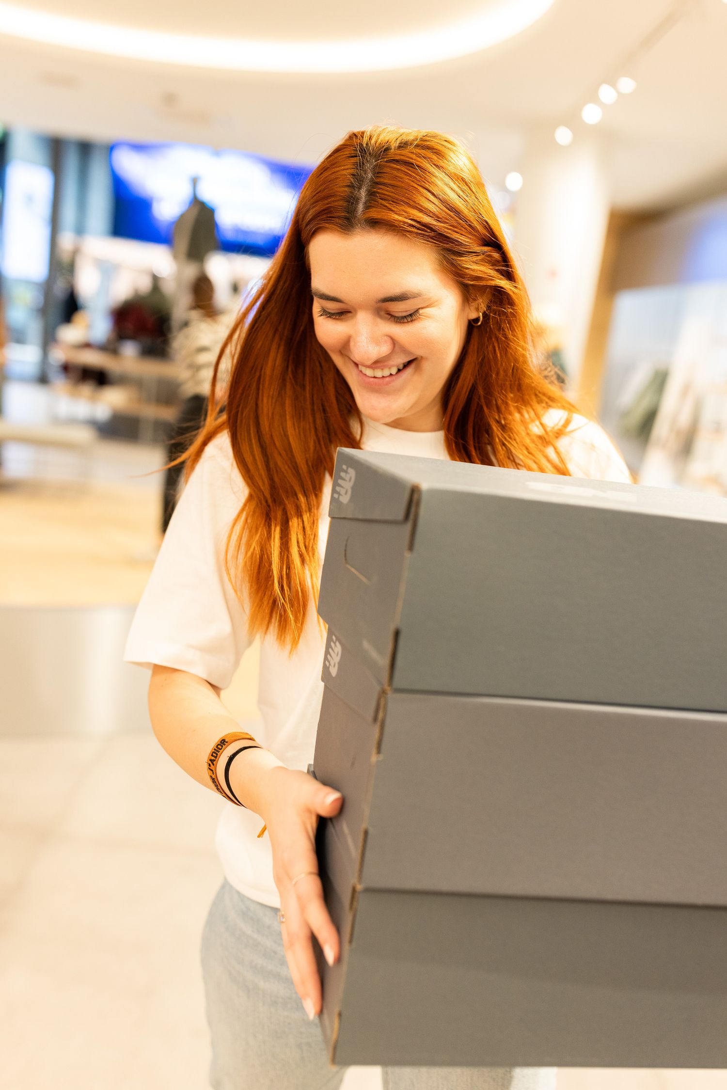 Woman in white shirt smiling while looking down at gray boxes in bright retail environment.