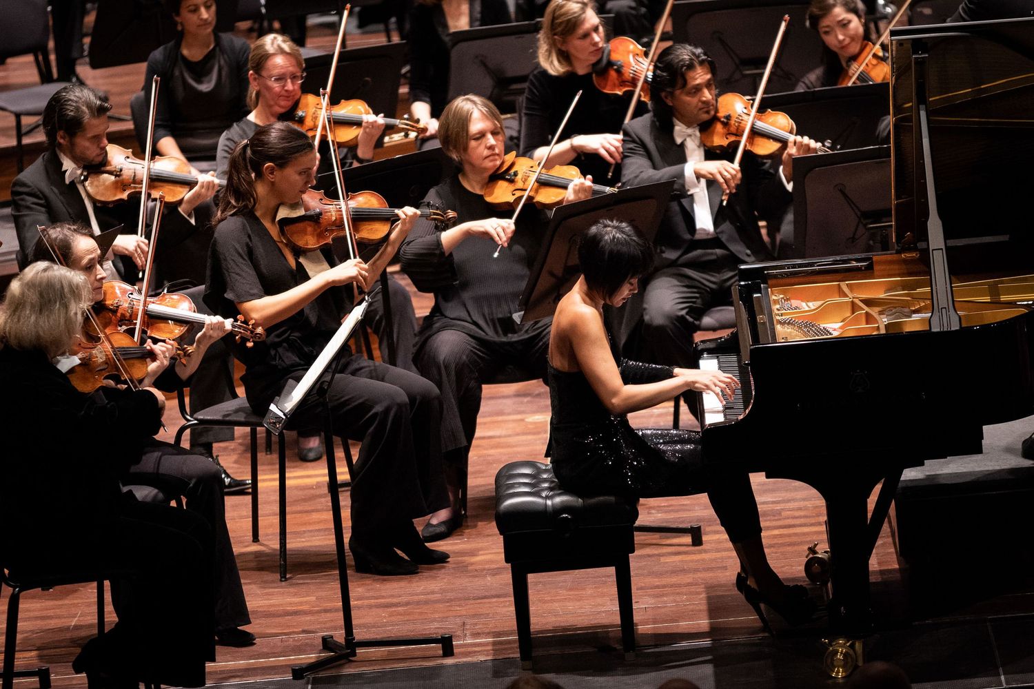 Symphony orchestra performs on stage with violinists in formal black attire playing in concert hall.