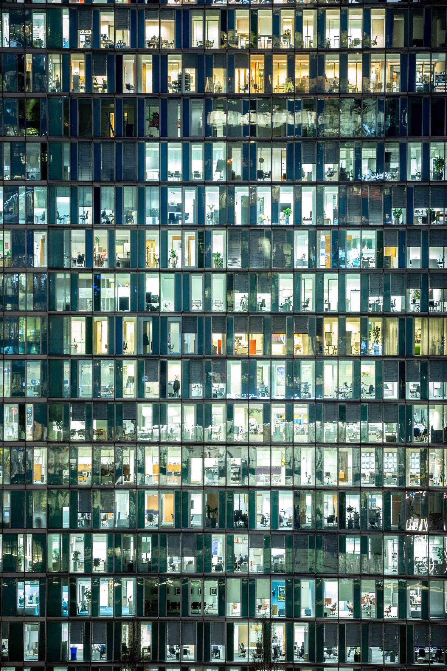 Office building facade at night with illuminated windows creating a grid pattern of lit workspaces in a modern skyscraper.