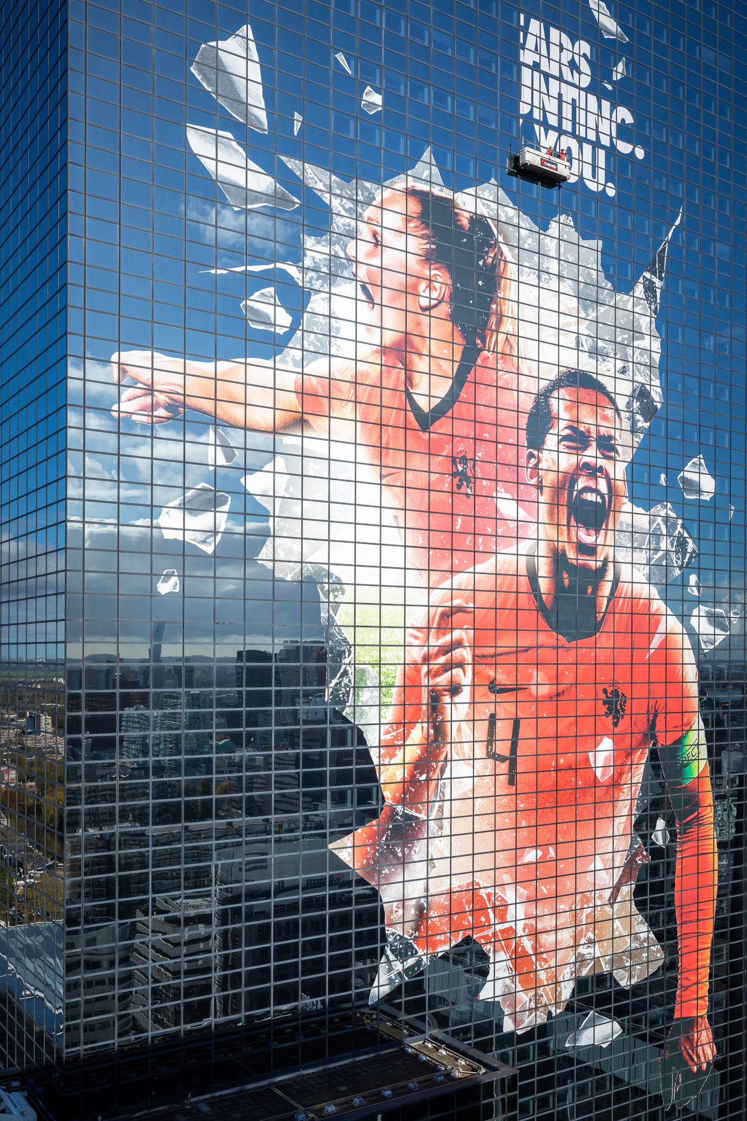Large mural of Dutch soccer players in orange jerseys displayed on a glass skyscraper facade.