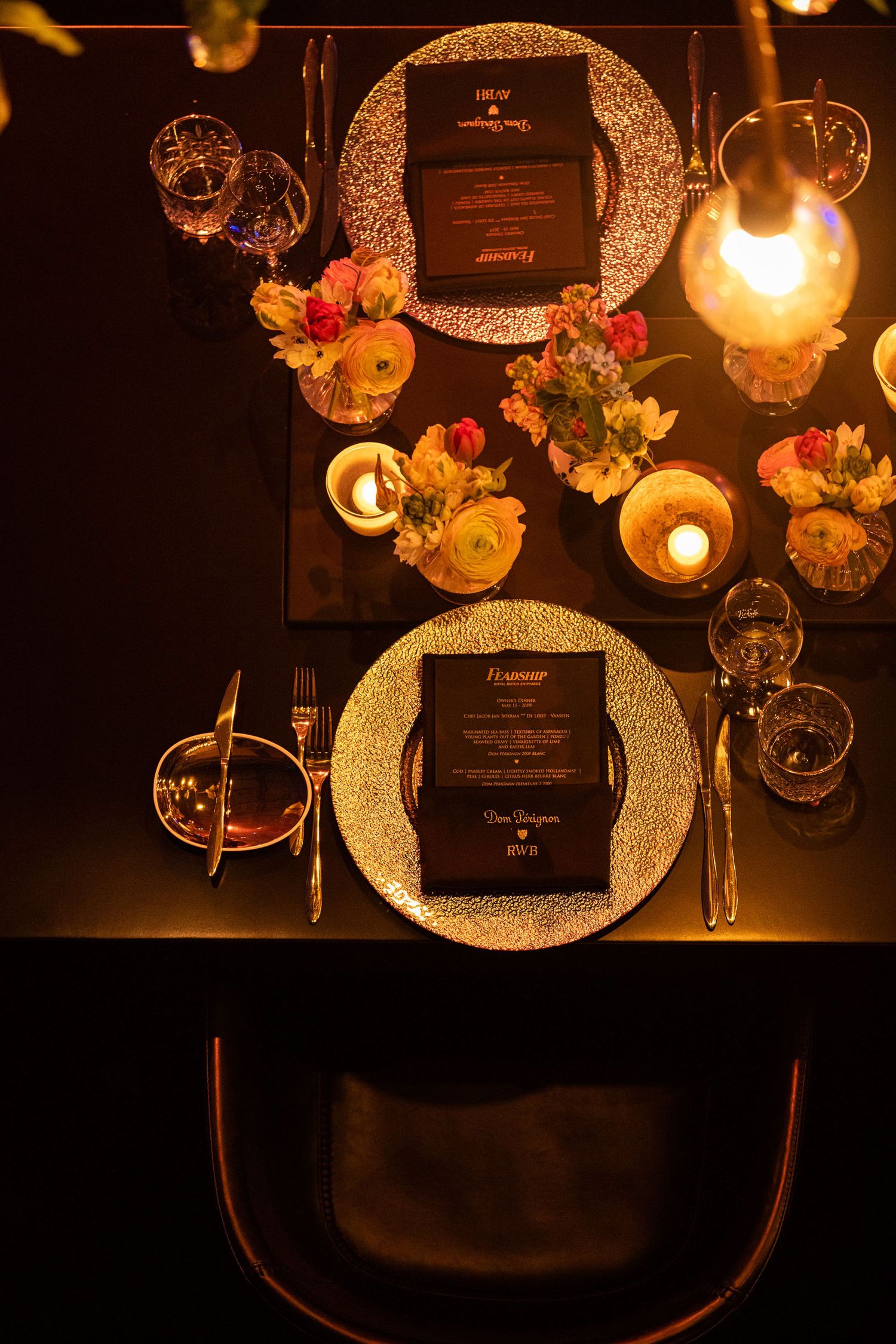 Elegant table setting with candlelight, textured charger plates, and menus in a dimly lit romantic restaurant atmosphere.