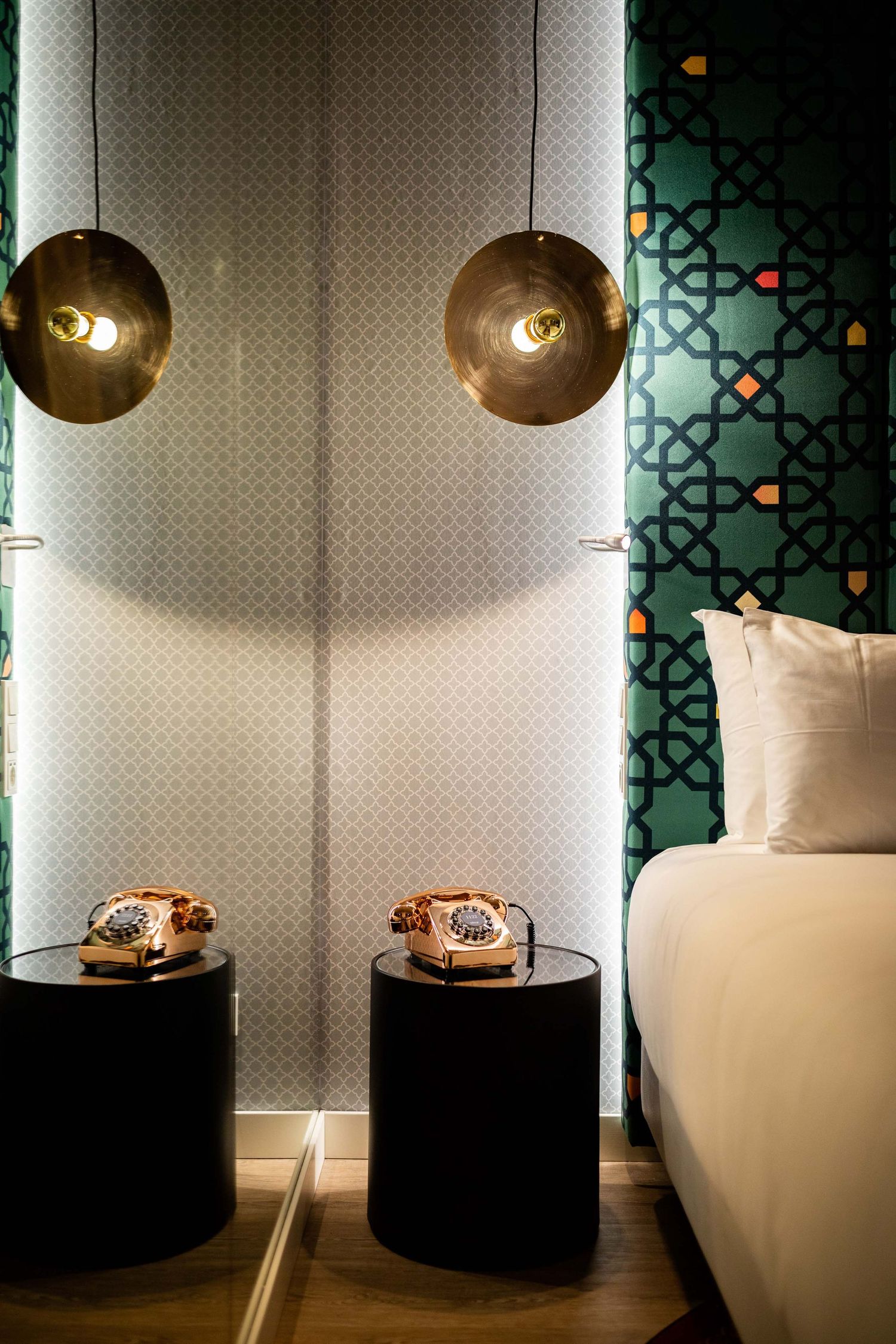 Modern hotel room interior with brass wall sconces, vintage rotary phones on black side tables, and geometric wallpaper.