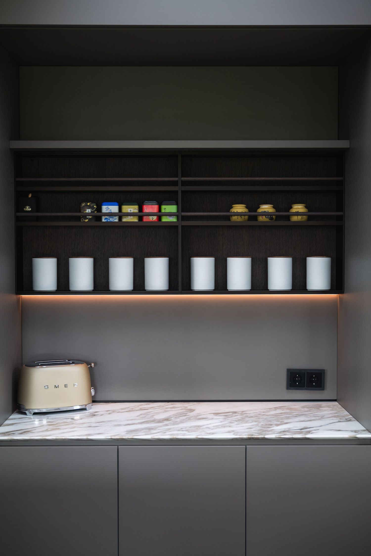 Modern kitchen shelving with white ceramic containers and colorful jars arranged neatly against a dark wall.