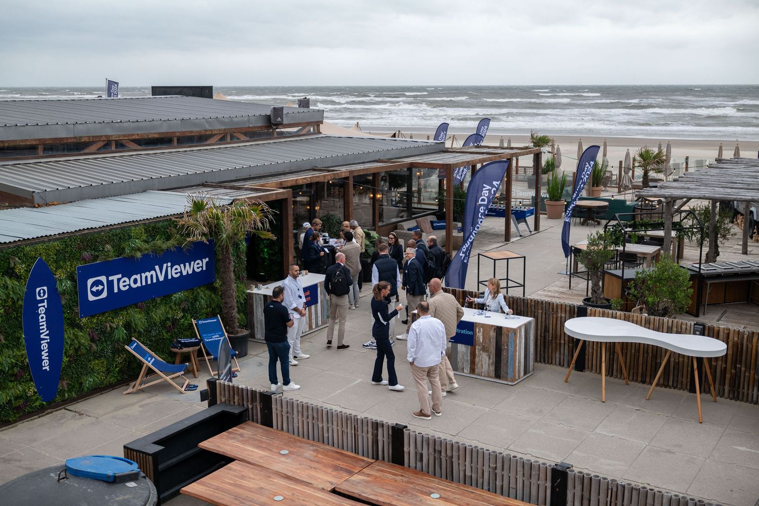 Outdoor beach event setup with branded banners and people gathering on a wooden deck.
