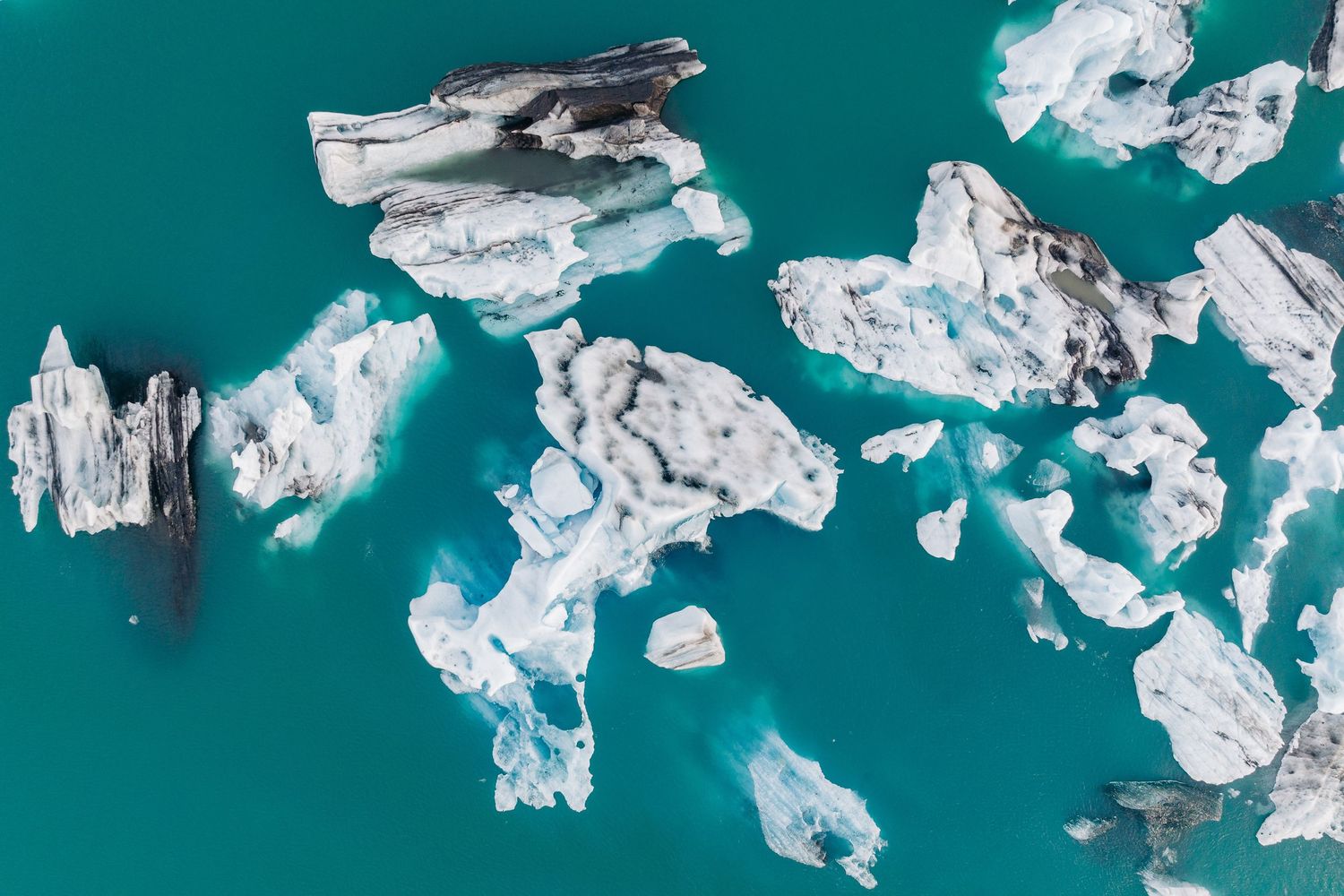 Aerial view of white icebergs floating in turquoise glacial water captured from above.