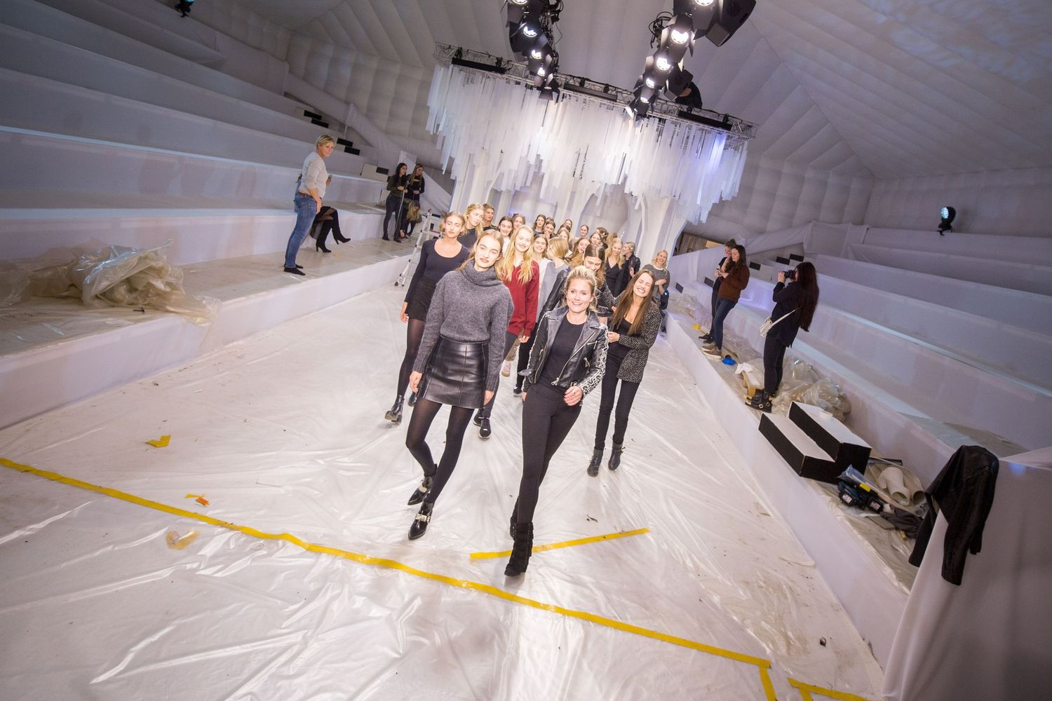 Models walk a white plastic runway inside an inflatable venue with hanging white fabric and stage lighting.