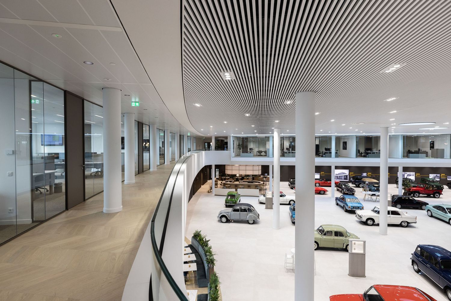 Modern car dealership showroom interior with luxury vehicles displayed on two levels and sleek architectural design.