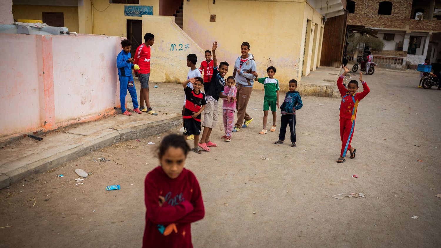 Children playing and gathering in a street of what appears to be a residential neighborhood.
