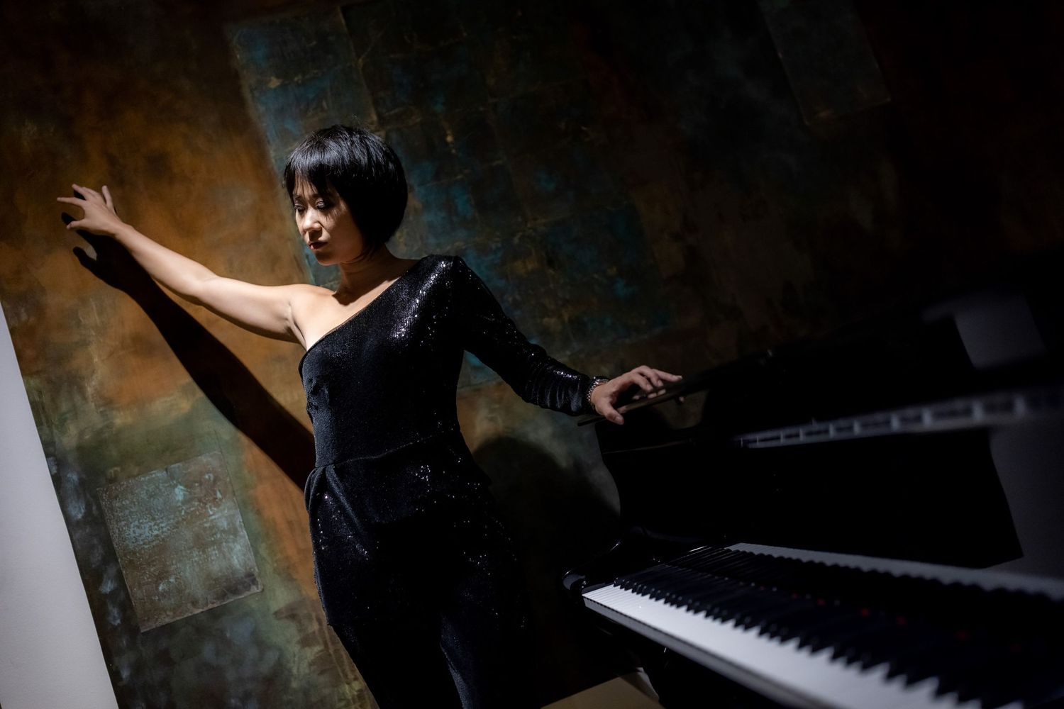 A person in a dark room plays an illuminated piano keyboard with dramatic lighting and shadows.