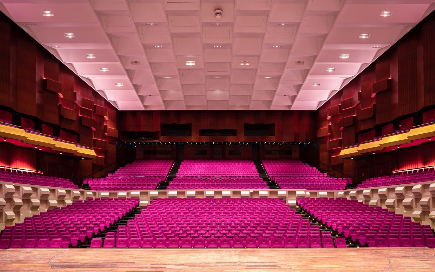 Panoramic view of a modern theater auditorium with pink lighting and rows of empty seats stretching across the space.