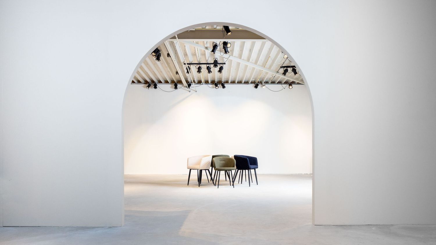 Minimalist white room with arched doorway and small dining set beneath industrial ceiling lights.