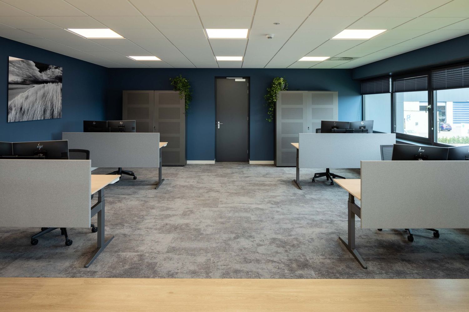 Modern office space with adjustable height desks, ergonomic chairs, and bright fluorescent lighting in an open floor plan layout.
