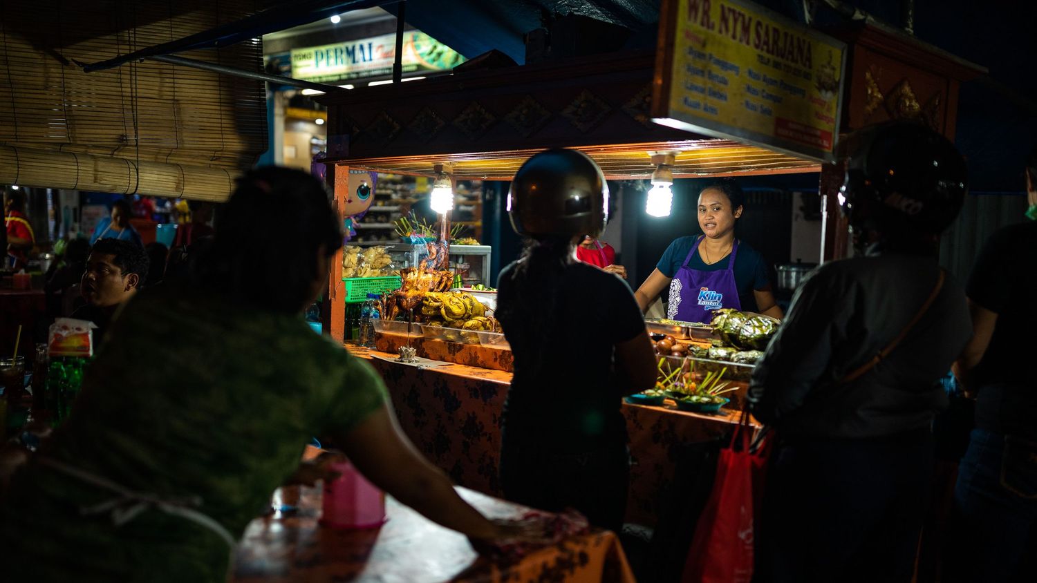 Dark atmospheric view of a street market with illuminated food stalls and vendors.