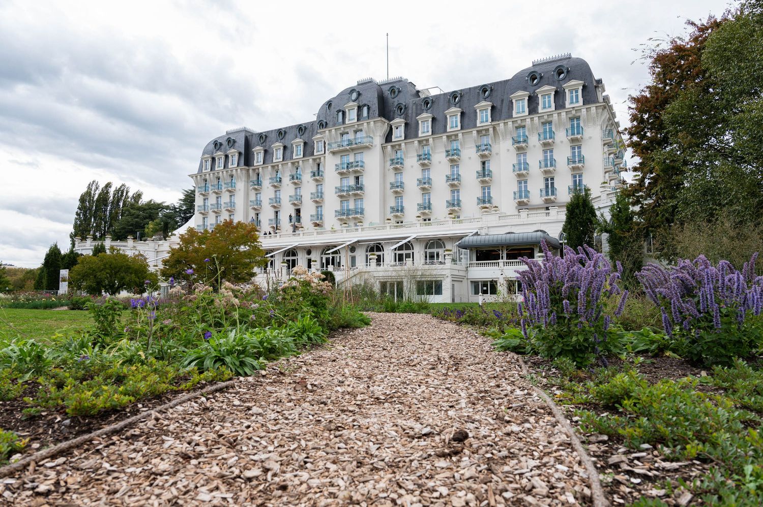 Historic stone hotel building with French architecture and purple flowers in the foreground.