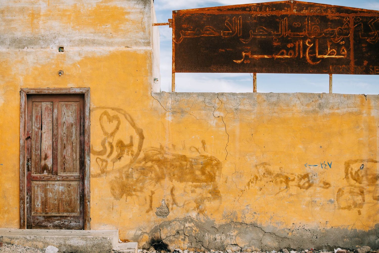Weathered yellow wall with Arabic text and windows in an old building.