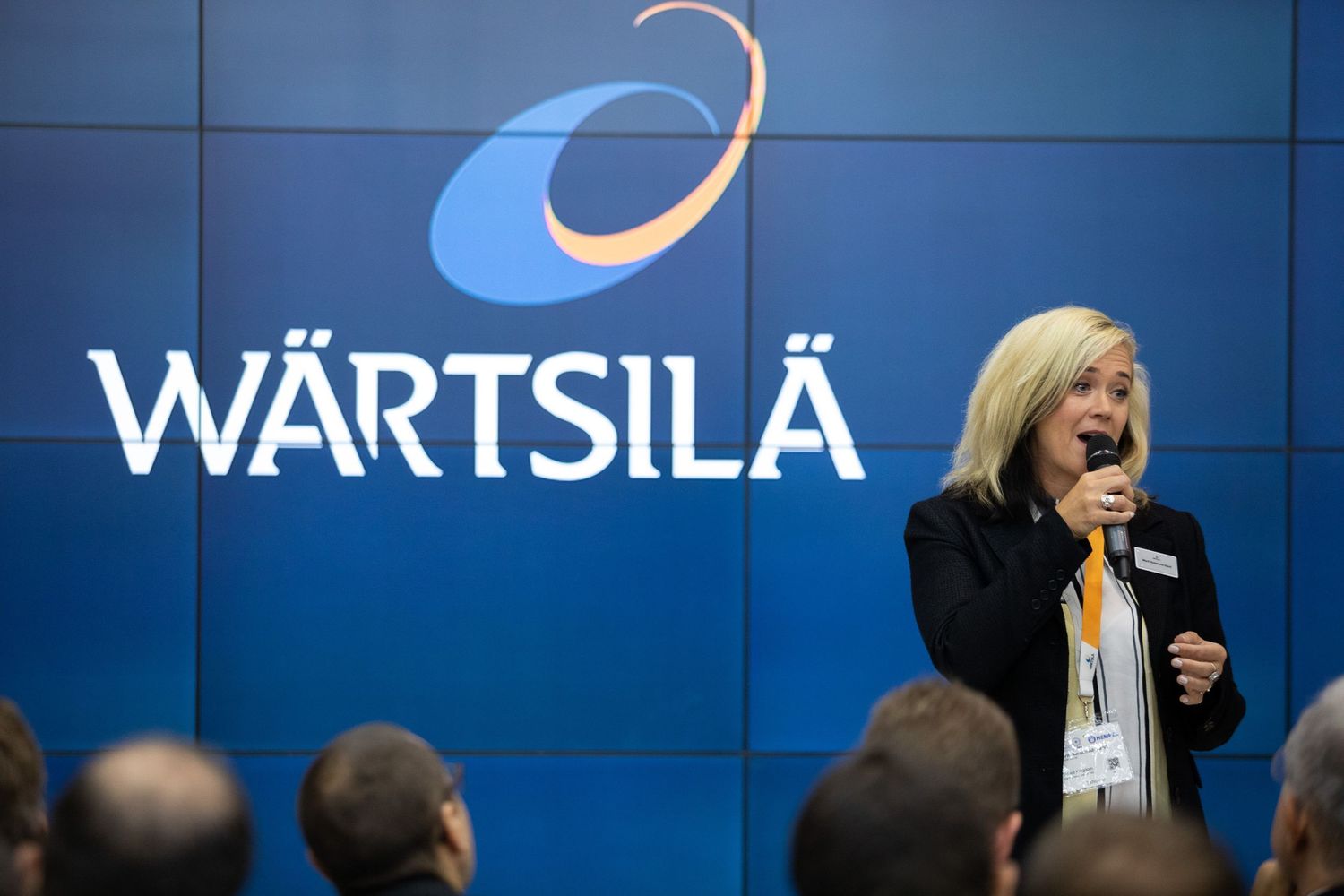 Group of people gathered at a corporate event with blue Wartsila branded backdrop panels visible.
