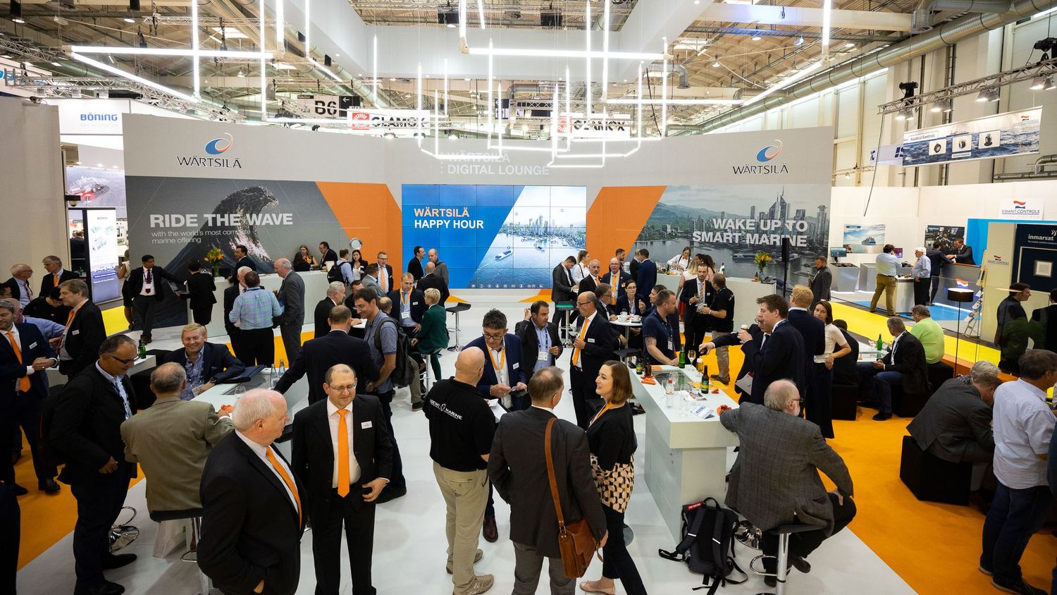 A crowded technology conference or trade show floor with attendees networking between colorful exhibition booths.