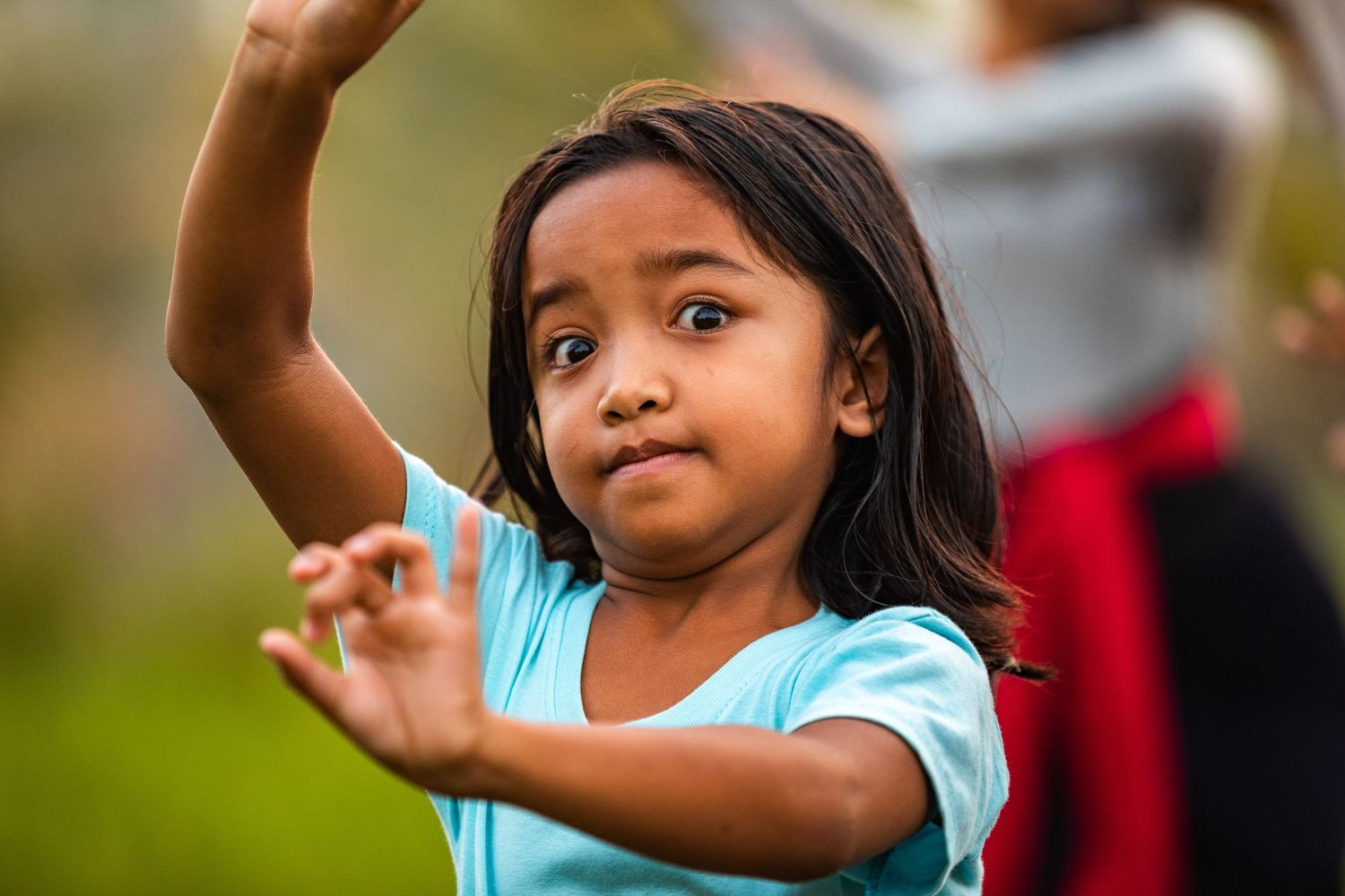 Dancer performs expressive hand movements against natural background.