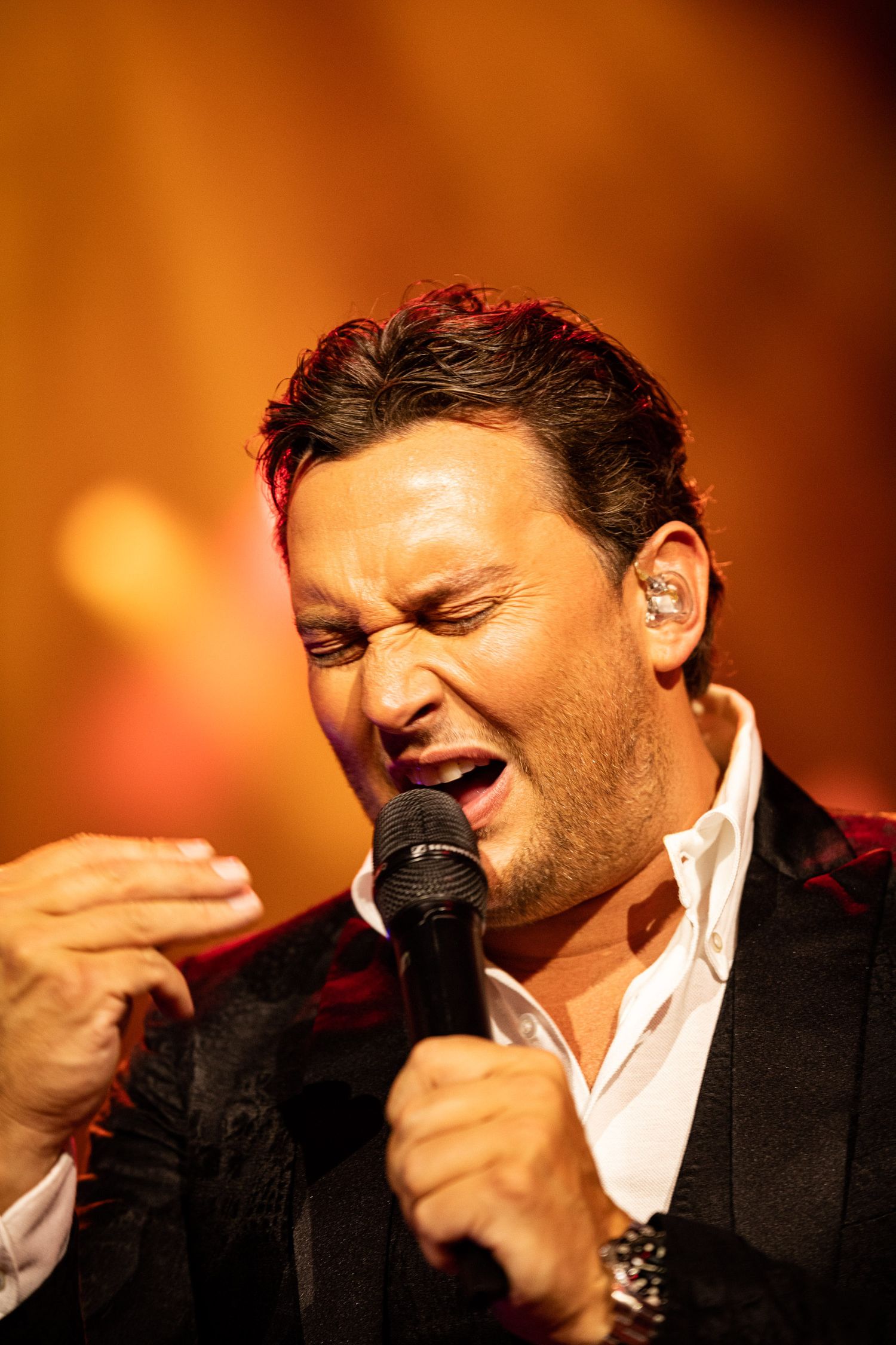 A sequence of photos showing a performer in a black suit passionately singing into a microphone against a warm orange background.