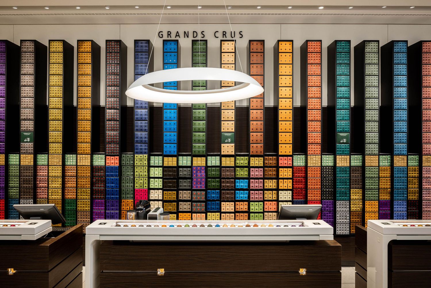 Colorful wall display of coffee capsules arranged in a rainbow gradient pattern.