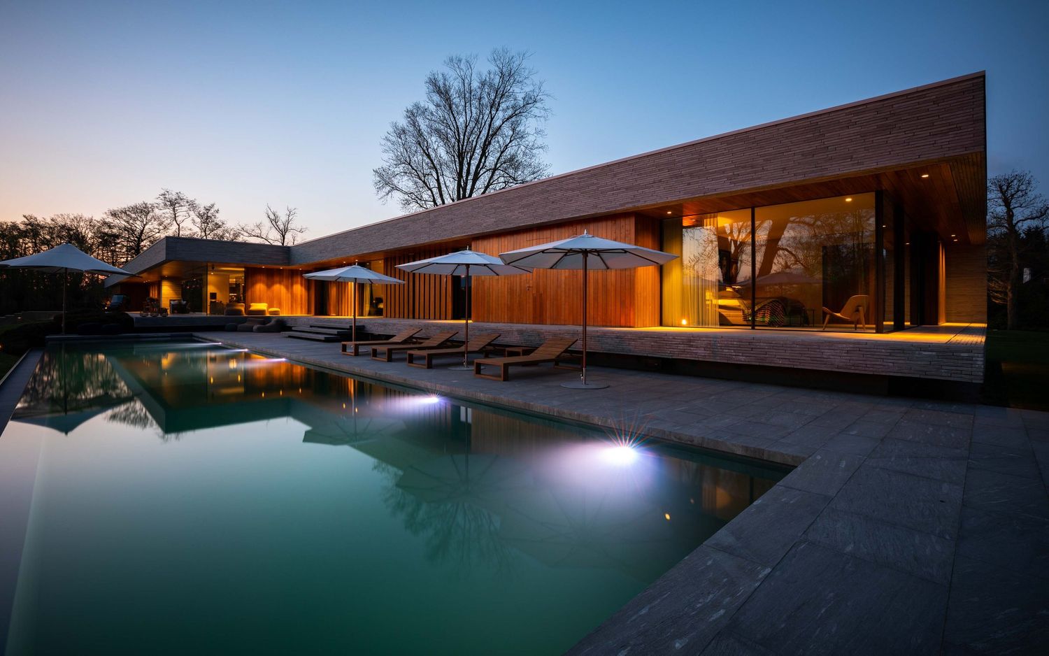 Illuminated swimming pool at dusk with modern architectural elements and glowing underwater lights creating a serene ambiance.