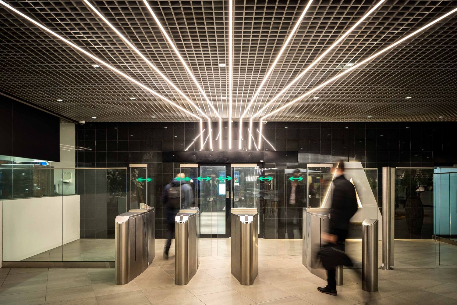 Modern subway station corridor with illuminated ceiling panels and sleek stainless steel turnstiles.