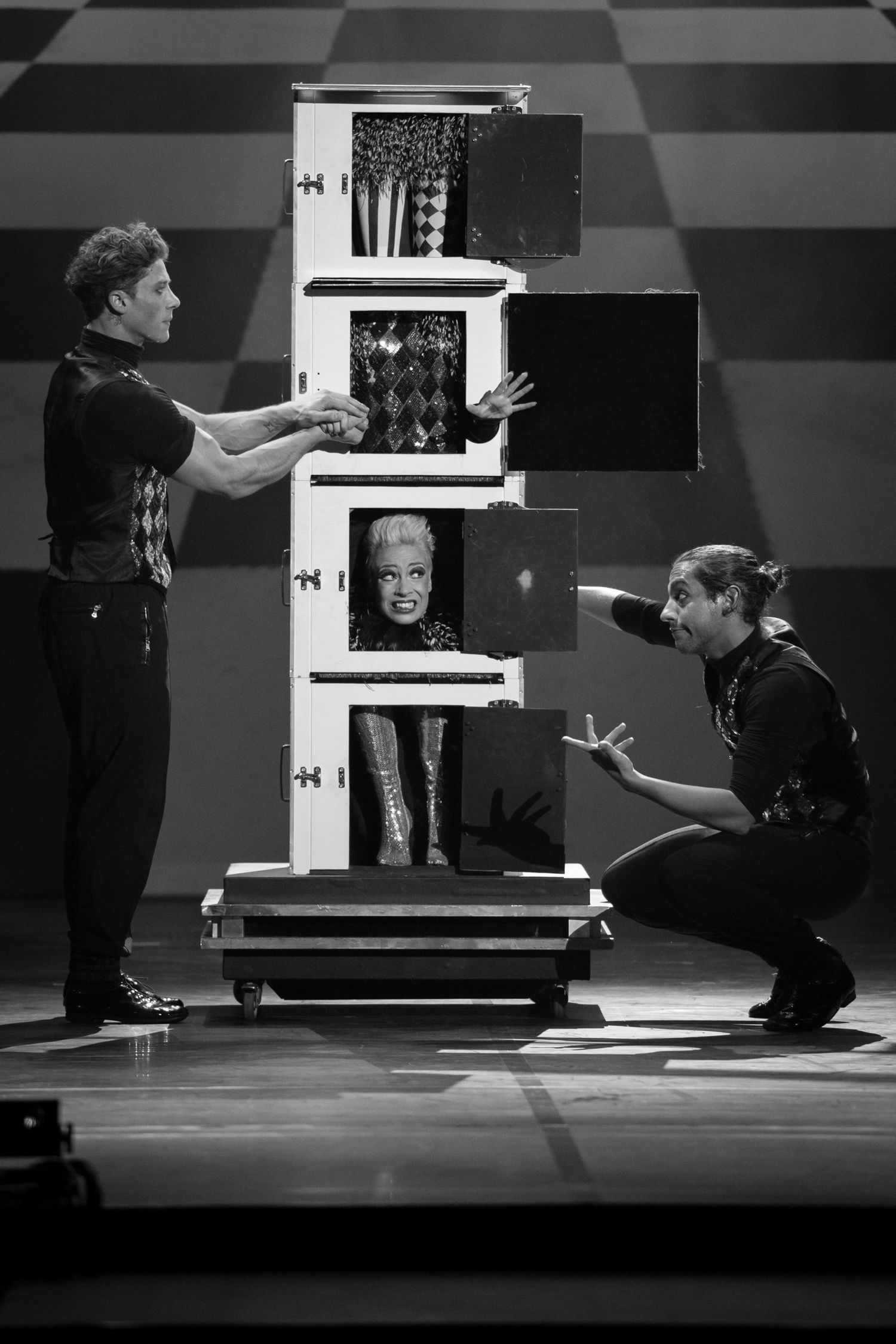 Black and white photo of two magicians performing a cabinet illusion trick on stage with a woman inside.