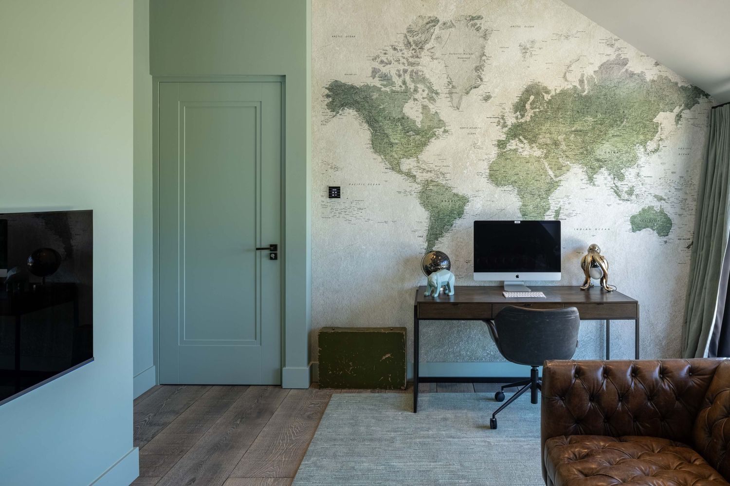 World map wallpaper decorates a minimalist room with mint green doors and hardwood flooring.