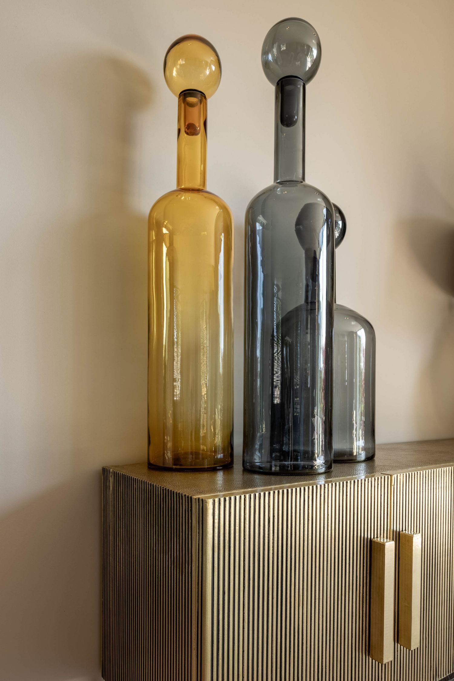 Two decorative glass bottles in amber and smoky gray colors sit atop a textured cabinet with brass handles.