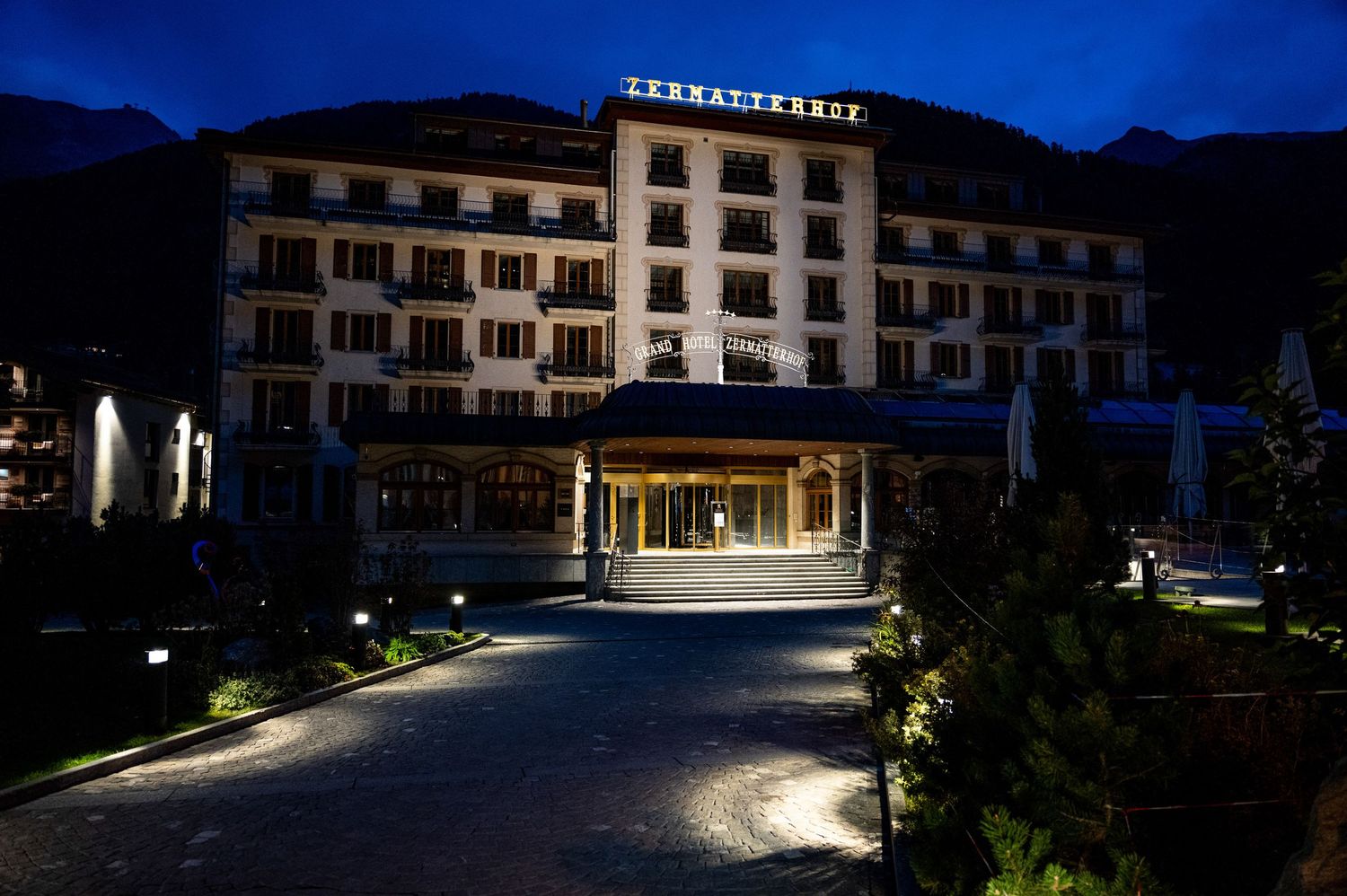 Hotel buildings lit up at night against mountain backdrop in alpine resort.