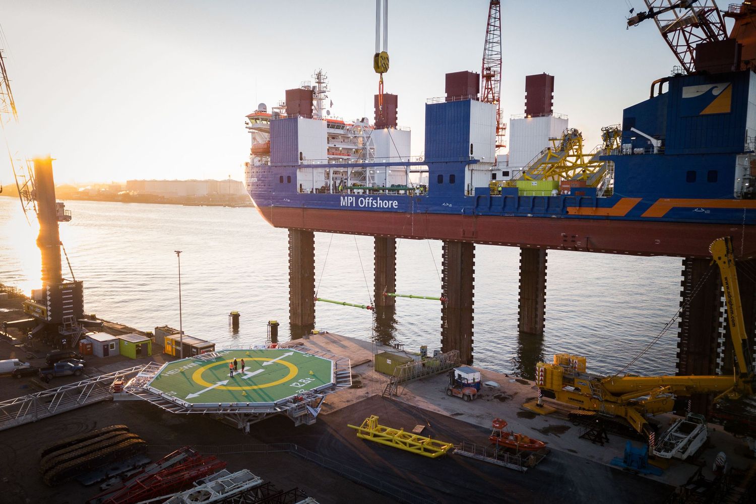 HVI Offshore vessel docked at port during sunset, featuring a helipad and large crane structure over water.