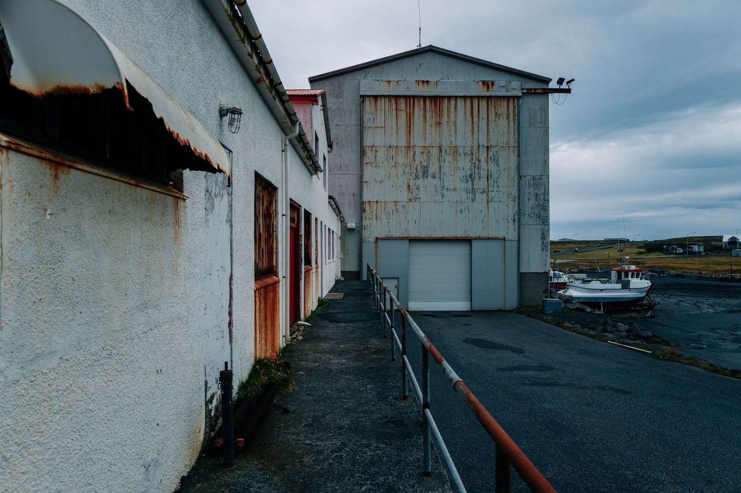 A series of connected boat storage buildings with white walls line a narrow path along a coastal harbor.