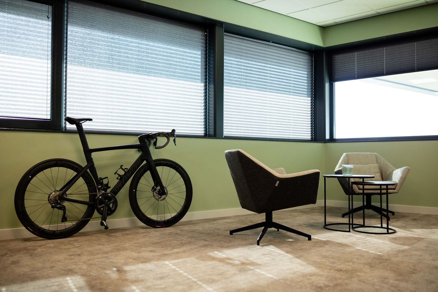 Modern office corner with sleek black road bike parked against mint green wall, featuring minimalist seating area.