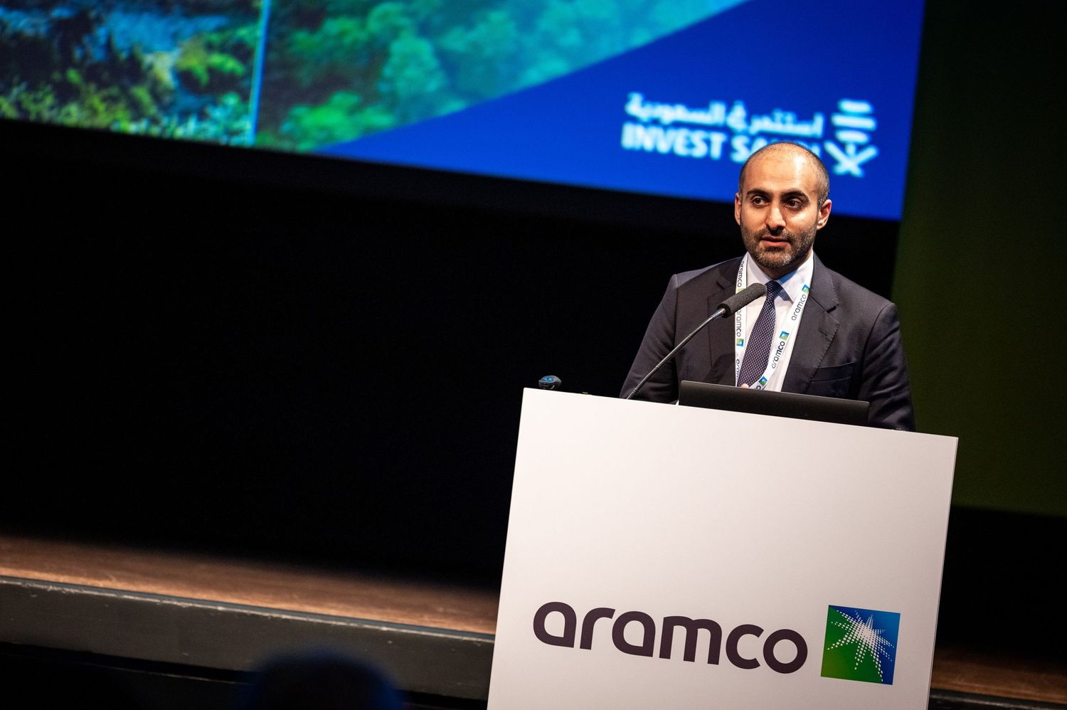 Corporate event stage setup with Aramco logo displayed on presentation screens.