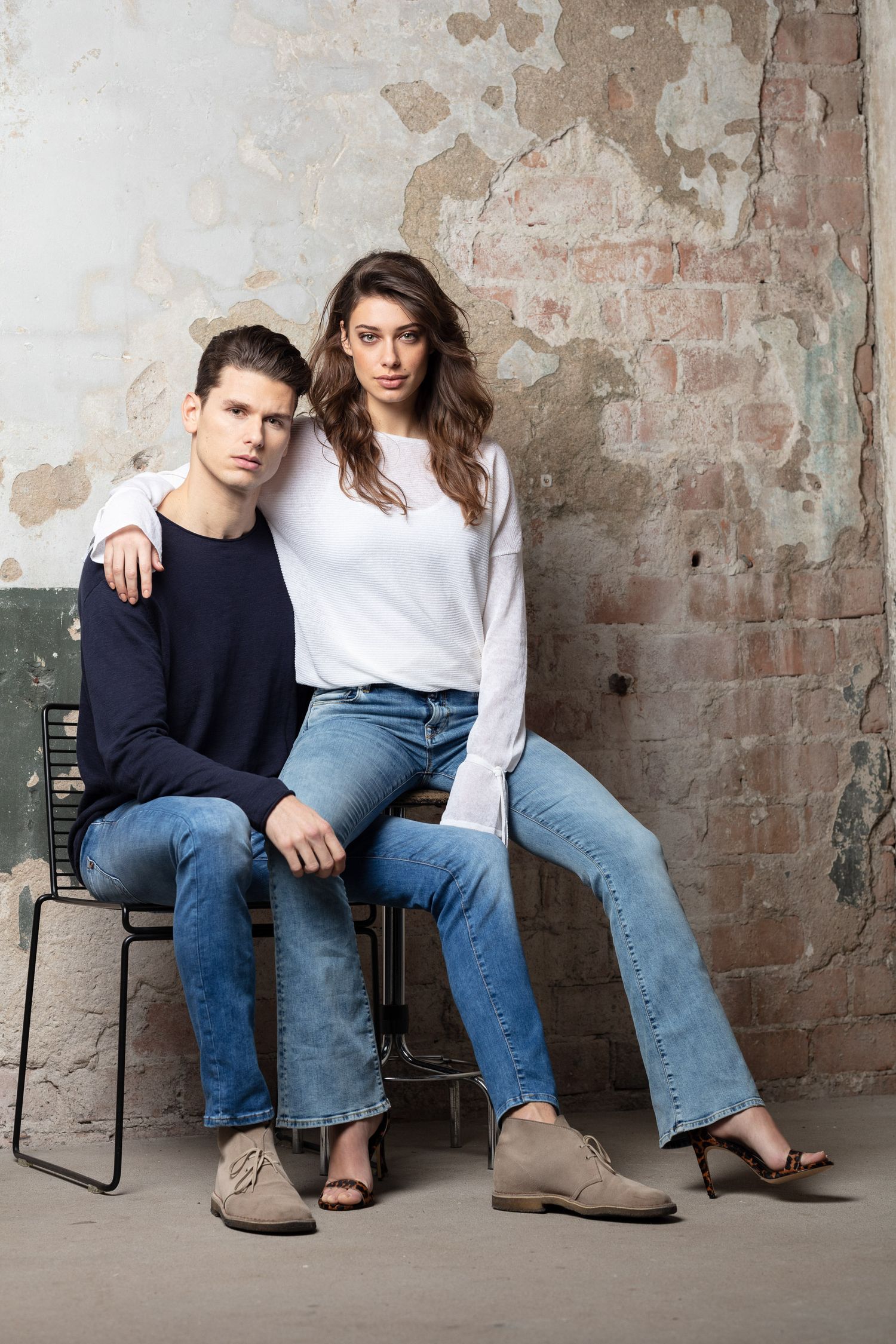 Casual fashion photo shoot against distressed brick wall featuring denim and contrasting dark and light tops.