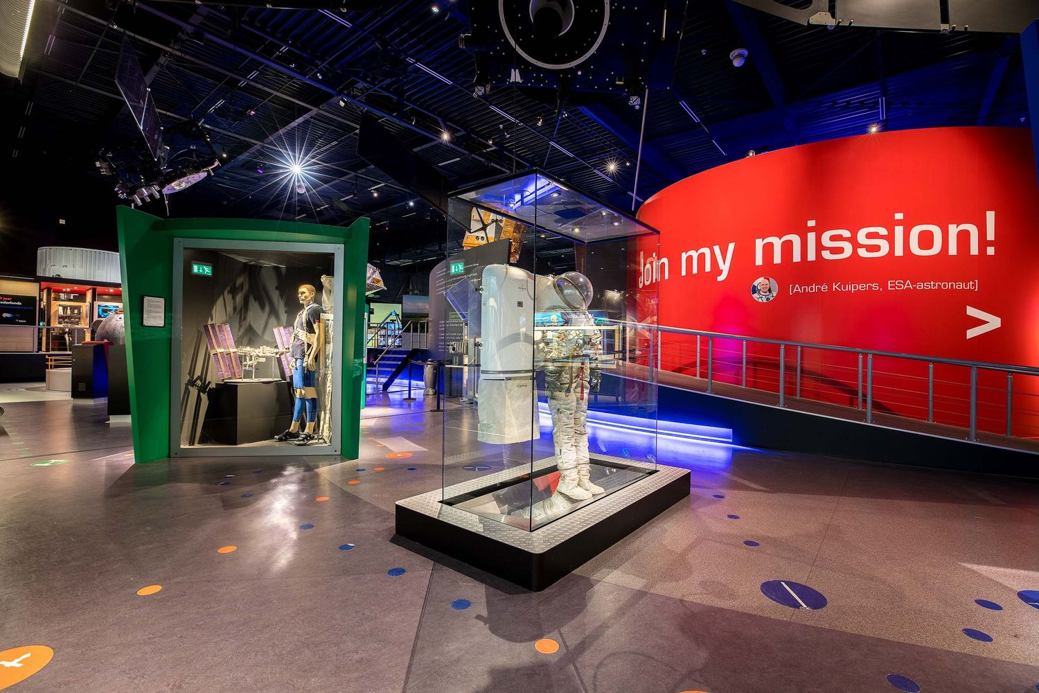 Interactive science museum exhibit with astronaut spacesuit display, glowing installations, and a red wall reading 'in my mission!'.