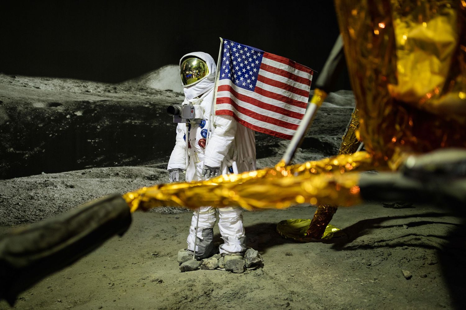 Astronaut in white spacesuit standing on the moon surface next to an American flag during a lunar mission.