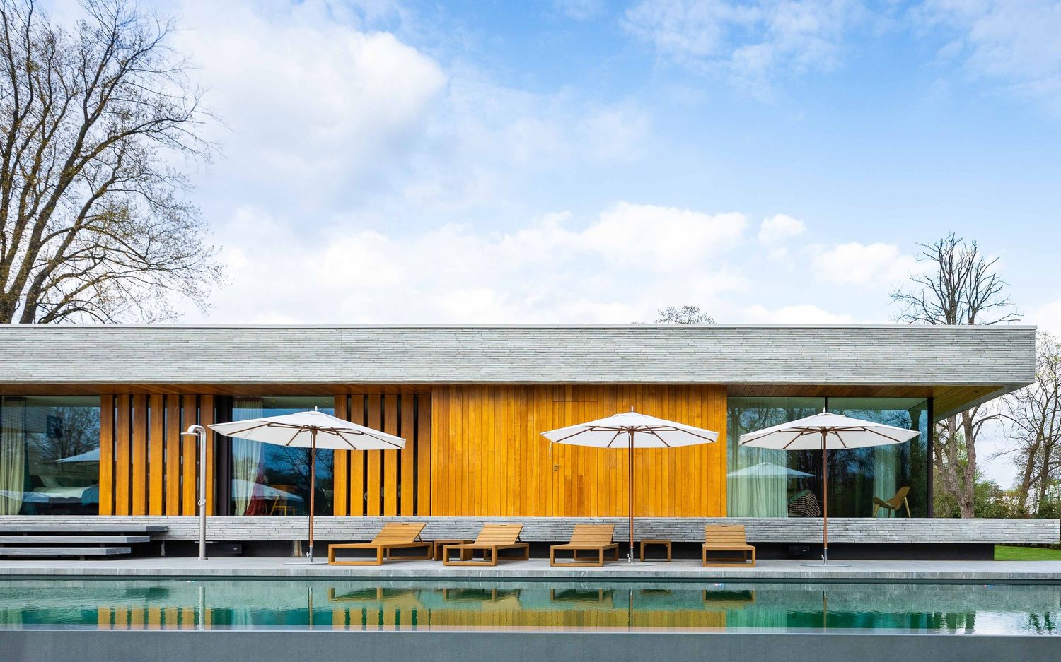 Long modern building with glass walls and wood accents features multiple white umbrellas on an outdoor patio area.