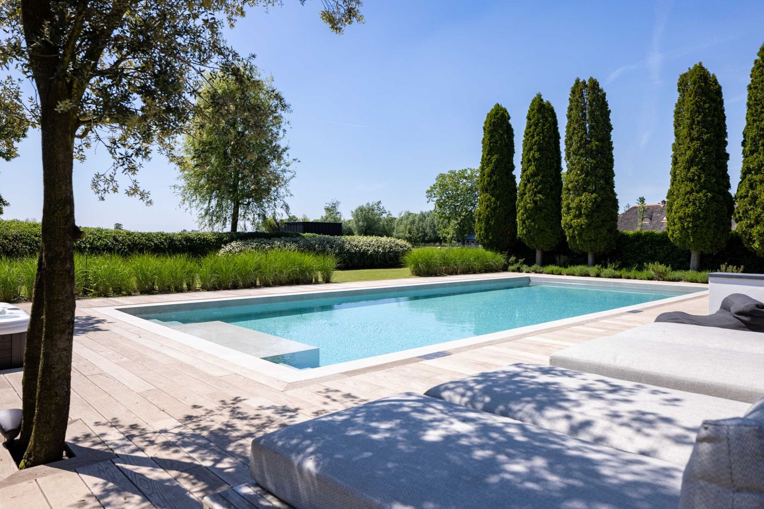 A long lap pool surrounded by cypress trees and manicured gardens stretches across a sunny Tuscan landscape.