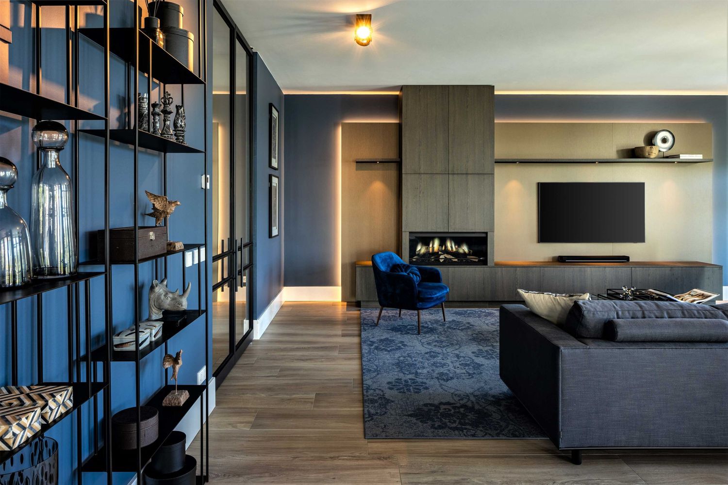Modern apartment interior with dark blue accents features sleek furniture and ambient lighting throughout connected living spaces.