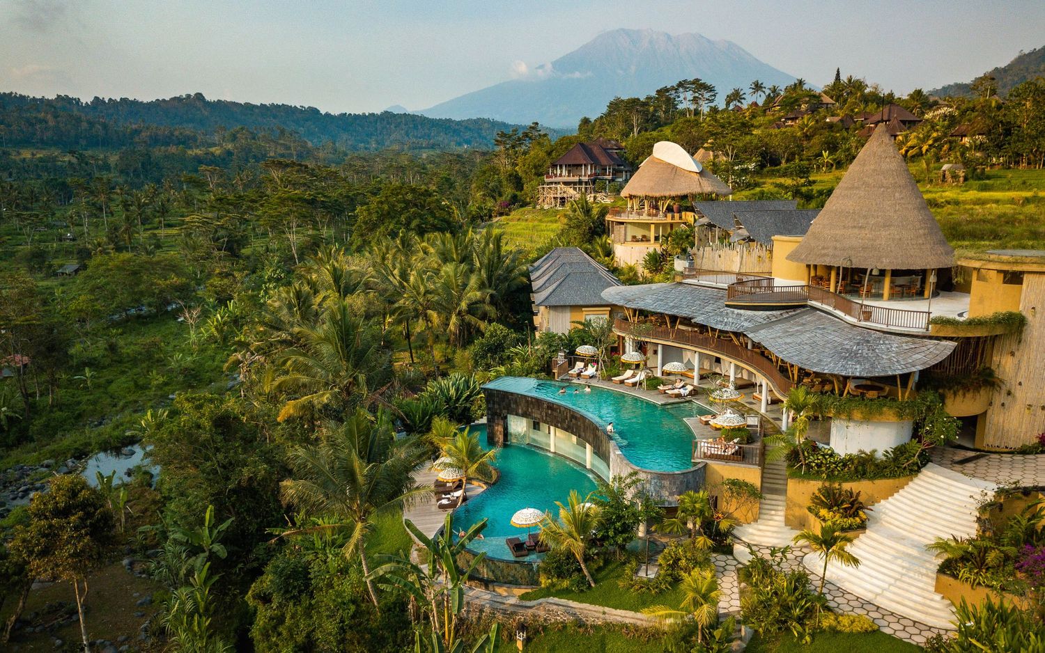 Aerial view of luxury resort with infinity pools nestled in tropical mountain landscape.