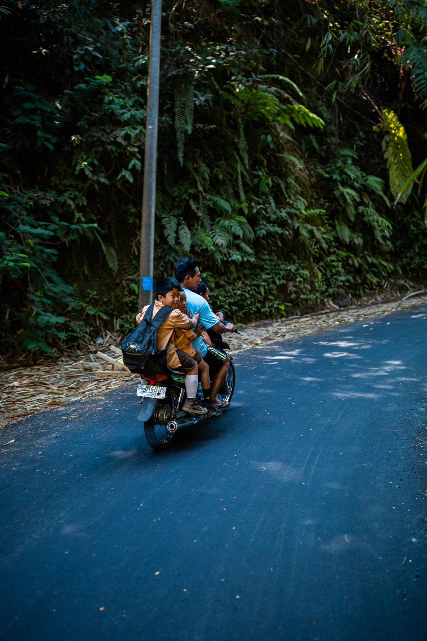 Sequence of motorcycle riders navigating a curved downhill road through tropical forest.