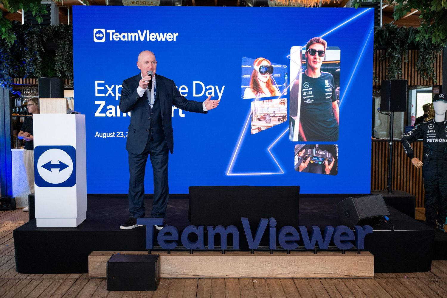 TeamViewer branded presentation stage with blue backdrop and digital displays.