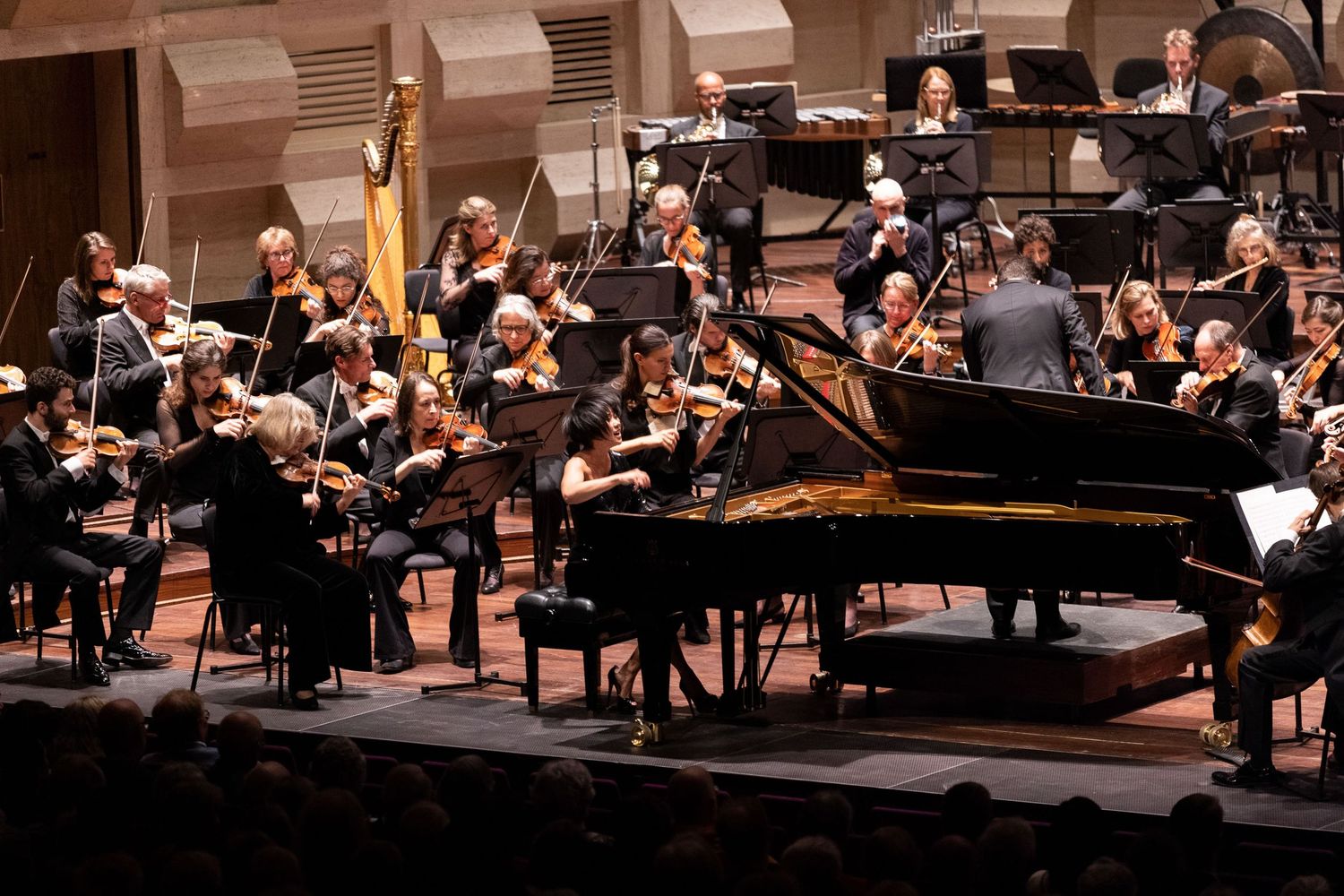 Classical musicians perform with a grand piano on stage during an orchestral concert at an elegant concert hall.